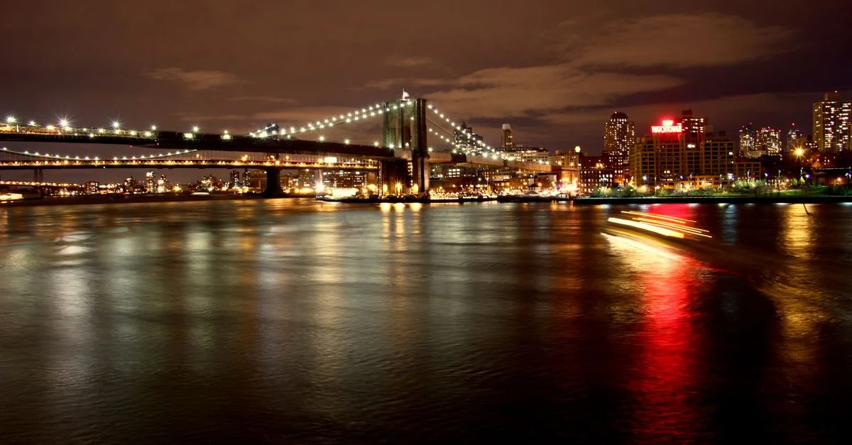 Escena nocturna cautivadora del Puente de Brooklyn con luces de la ciudad reflejándose en el río.