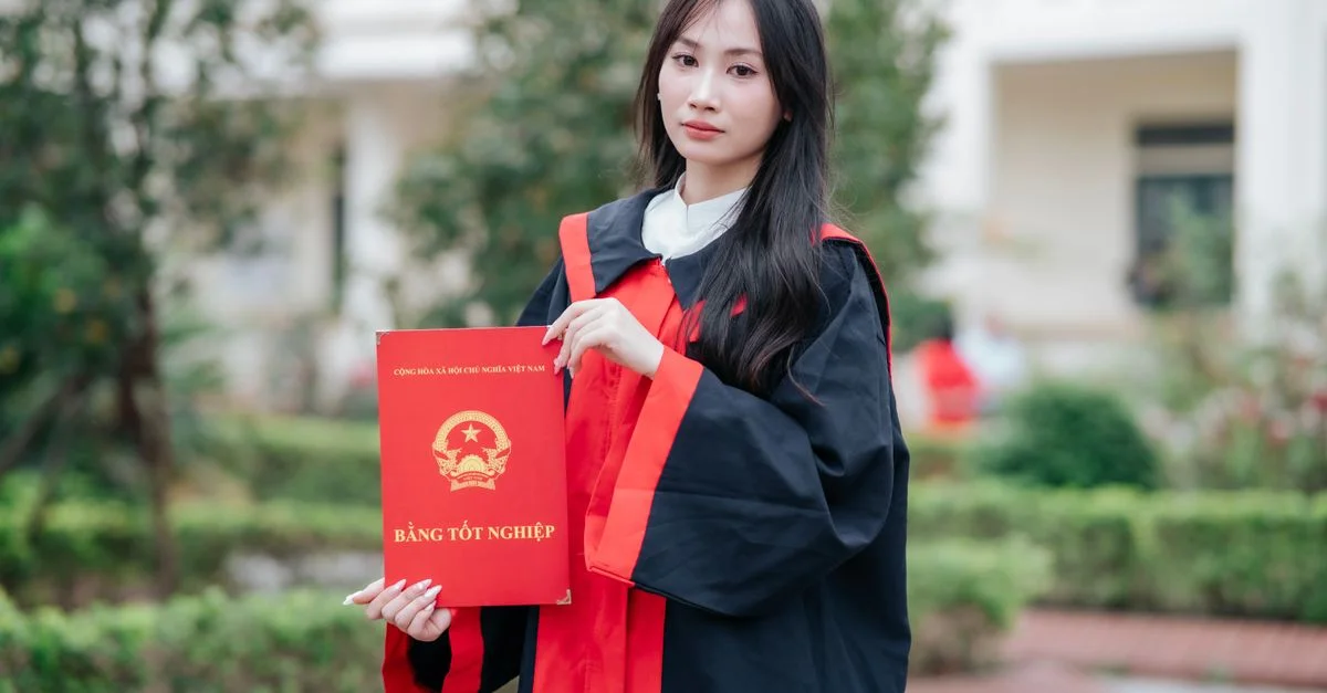 Jeune femme en robe de graduation tenant un diplôme en plein air, symbolisant la réussite.