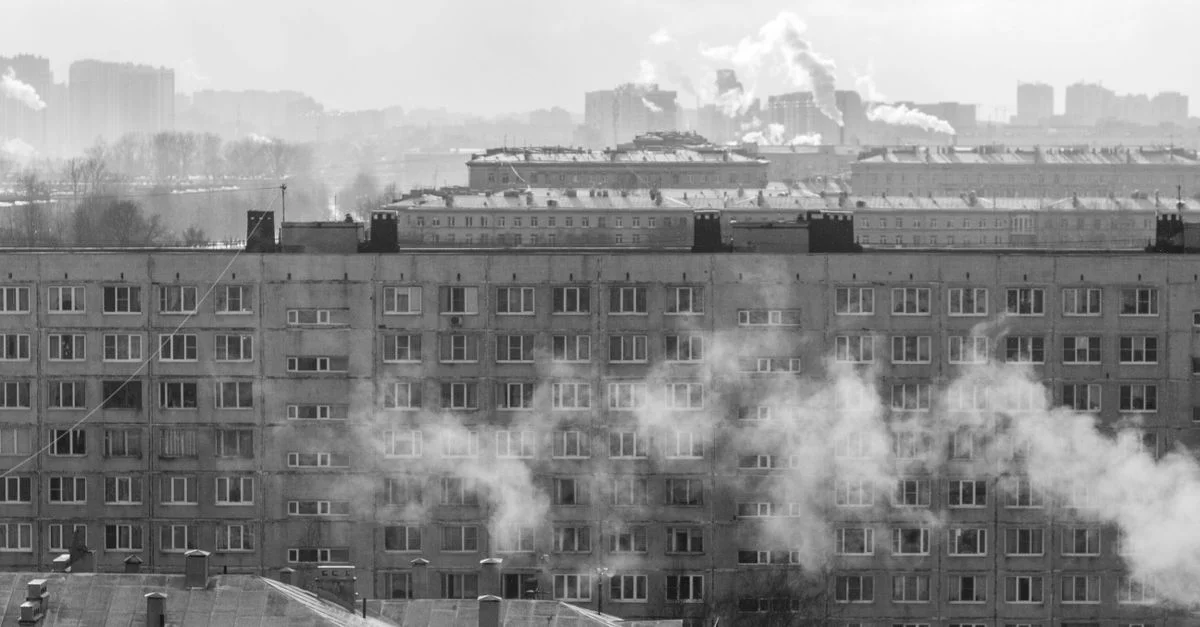 Foto en blanco y negro que muestra edificios residenciales urbanos con humo en el horizonte.