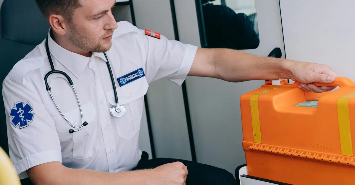 Paramédico sentado en una ambulancia con un kit médico naranja, listo para la respuesta a emergencias.