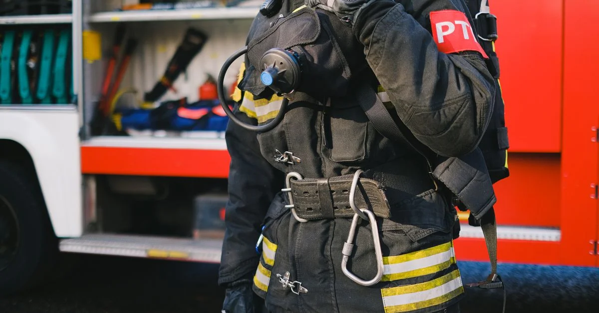 Un bombero con equipo de protección está listo junto a un camión de bomberos, mostrando preparación para emergencias.