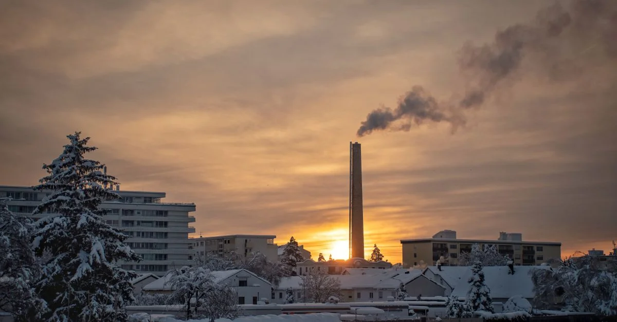 Serena vista urbana de invierno al amanecer con una chimenea humeante entre edificios nevados.