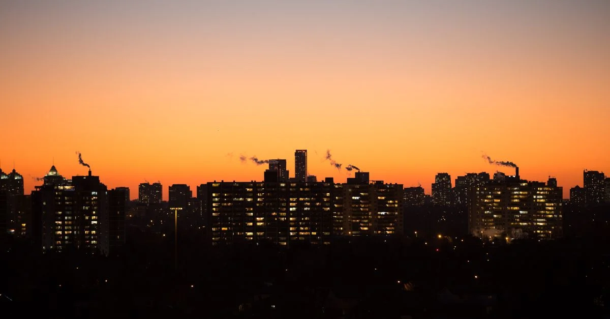 Silhouette del horizonte de la ciudad al anochecer con un vibrante cielo naranja y ventanas iluminadas.